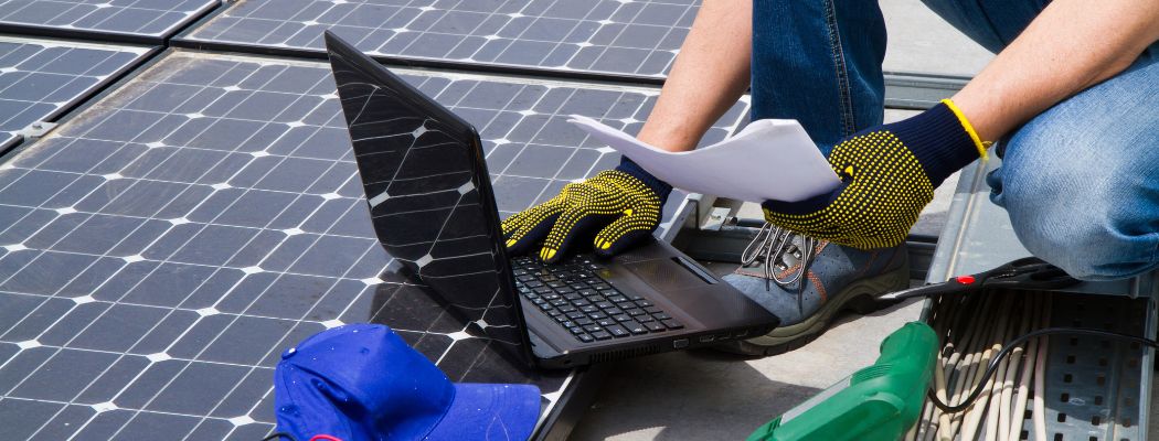 Mann mit Laptop auf Solardach berechnet etwas