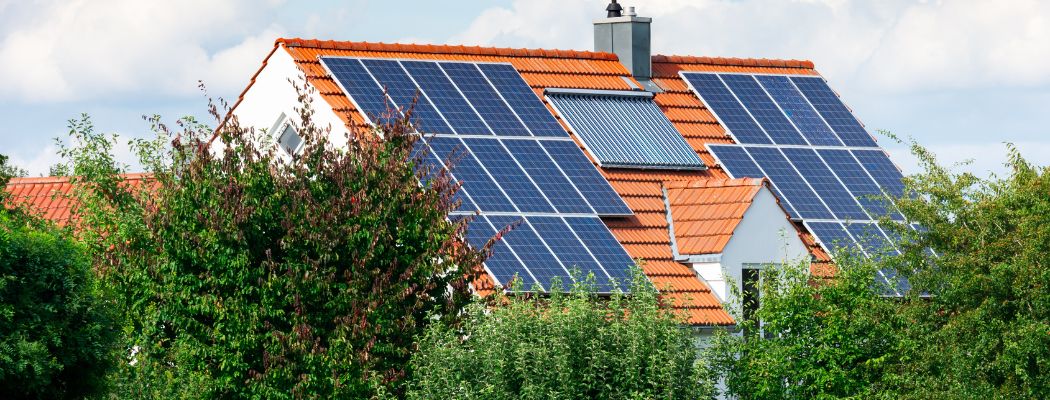 Hausdach mit Solarmodulen und Solarthermie. Davor gr&uuml;ne B&auml;ume